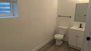 Half bath featuring wood finished floors, toilet, vanity, and baseboards