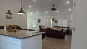 Kitchen featuring open floor plan, ceiling fan, wood finished floors, white cabinets, and recessed lighting