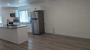 Kitchen featuring stainless steel appliances, a sink, dark wood-type flooring, white cabinetry, and baseboards