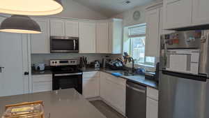 Kitchen featuring appliances with stainless steel finishes, a sink, vaulted ceiling, white cabinetry, and wood finished floors