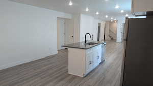 Kitchen with freestanding refrigerator, a sink, dark countertops, stainless steel dishwasher, and light wood-type flooring