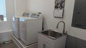 Laundry area with washer and dryer, wood finished floors, electric panel, and cabinet space