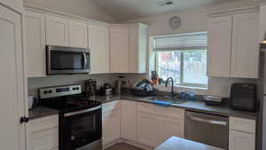 Kitchen featuring stainless steel appliances, a sink, lofted ceiling, and white cabinetry