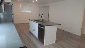 Kitchen featuring stainless steel appliances, a sink, a center island with sink, light wood finished floors, and dark countertops