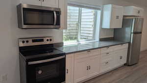 Kitchen with appliances with stainless steel finishes, light wood-style floors, white cabinets, and healthy amount of natural light