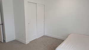 Unfurnished bedroom featuring light carpet, a closet, and baseboards