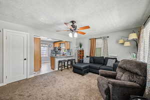 Living room featuring ceiling fan, light colored carpet, a textured ceiling, and baseboards