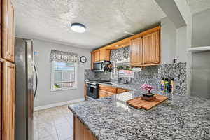 Kitchen with appliances with stainless steel finishes, a sink, backsplash, stone countertops, and baseboards