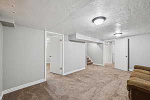 Finished basement with carpet, a textured ceiling, baseboards, and stairs