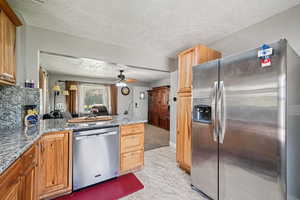 Kitchen featuring stainless steel appliances, a textured ceiling, a ceiling fan, and light stone counters