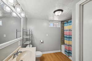 Bathroom featuring toilet, wood finished floors, a sink, baseboards, and a textured ceiling