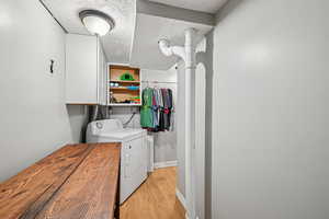 Laundry area with light wood finished floors, washer and clothes dryer, cabinet space, and baseboards