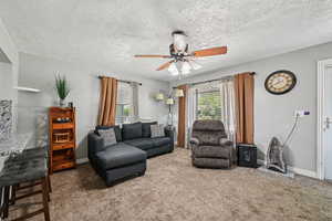 Living room with ceiling fan, carpet flooring, a textured ceiling, and baseboards