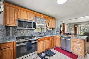 Kitchen with stainless steel appliances, a sink, tasteful backsplash, and light stone countertops