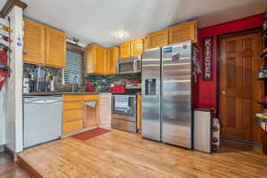 Kitchen featuring appliances with stainless steel finishes, light wood-style flooring, backsplash, and a sink