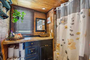 Bathroom featuring wooden walls, vanity, curtained shower, and wood ceiling