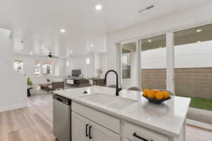 Kitchen with stainless steel dishwasher, a sink, open floor plan, LVP flooring, and white cabinets