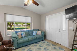 Living room featuring a ceiling fan, vaulted ceiling, and carpet flooring
