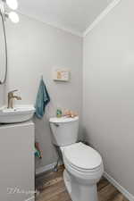 Bathroom featuring wood finished floors, toilet, baseboards, ornamental molding, and vanity