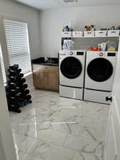 Laundry room with light marble finish floors, washer and clothes dryer, and a sink