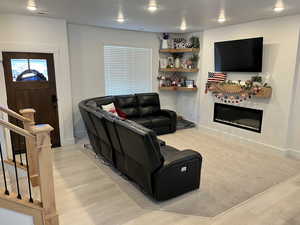 Living area featuring a glass covered fireplace, light wood finished floors, stairway, baseboards, and recessed lighting