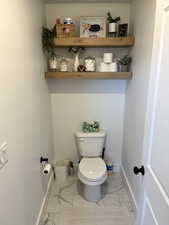 Bathroom with marble look tile flooring, toilet, and baseboards