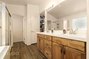 Full bathroom featuring a shower stall, double vanity, wood finished floors, a bath, and lofted ceiling