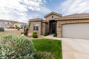 View of front facade featuring concrete driveway, stucco siding, a garage, stone siding, and a tile roof