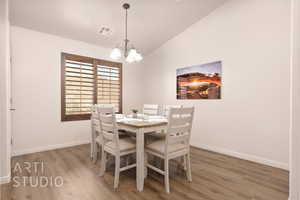 Dining room featuring wood finished floors, vaulted ceiling, baseboards, and a chandelier