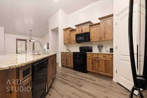 Kitchen with black appliances, a sink, wood finished floors, light stone countertops, and brown cabinetry