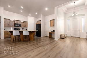 Kitchen featuring black appliances, a kitchen bar, wood finished floors, a center island with sink, and recessed lighting