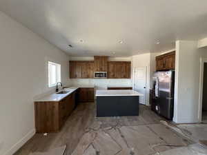 Kitchen featuring stainless steel appliances, a sink, a kitchen island, brown cabinets, and light wood finished floors