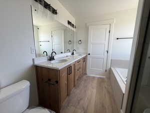 Bathroom featuring wood finished floors, double vanity, a garden tub, and toilet