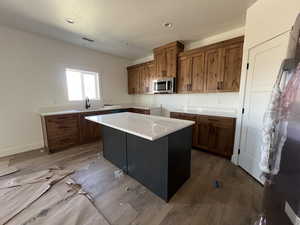 Kitchen with stainless steel microwave, a sink, brown cabinetry, hardwood / wood-style floors, and a center island