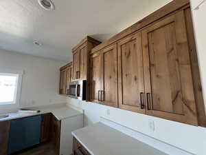 Kitchen with brown cabinets, stainless steel microwave, dishwasher, a textured ceiling, and light countertops