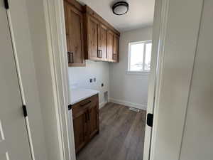 Washroom featuring hookup for an electric dryer, hookup for a washing machine, cabinet space, dark wood-type flooring, and baseboards