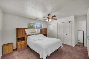 Carpeted bedroom featuring multiple closets, a textured ceiling, ceiling fan, and baseboards