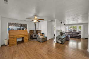 Living room featuring a textured ceiling, a wood stove, wood finished floors, and ceiling fan