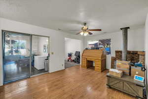 Misc room with a textured ceiling, a wood stove, wood finished floors, and ceiling fan