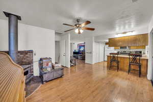 Living room with a wood stove, a ceiling fan, light wood-style floors, and a textured ceiling