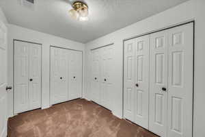 Unfurnished bedroom with carpet, a textured ceiling, and multiple closets