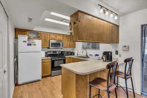 Kitchen with appliances with stainless steel finishes, a sink, a peninsula, light wood finished floors, and light countertops