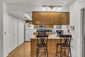 Kitchen with appliances with stainless steel finishes, a peninsula, light countertops, light wood-style floors, and a sink
