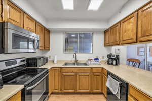 Kitchen featuring stainless steel appliances, a sink, light countertops, and brown cabinetry