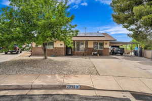 View of front facade featuring brick siding, solar panels, driveway, and an attached carport