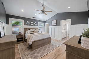 Bedroom featuring a wainscoted wall, a decorative wall, light wood-type flooring, vaulted ceiling, and ceiling fan