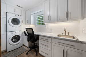 Washroom with stacked washer / drying machine, cabinet space, and wood finished floors