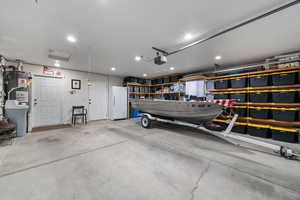 Garage with freestanding refrigerator, a garage door opener, gas water heater, and recessed lighting