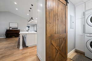 Laundry area featuring estacked washer and dryer, a barn door, cabinet space, light wood-style flooring, and recessed lighting