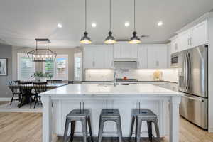 Kitchen featuring appliances with stainless steel finishes, a sink, light wood-style floors, tasteful backsplash, and white cabinetry